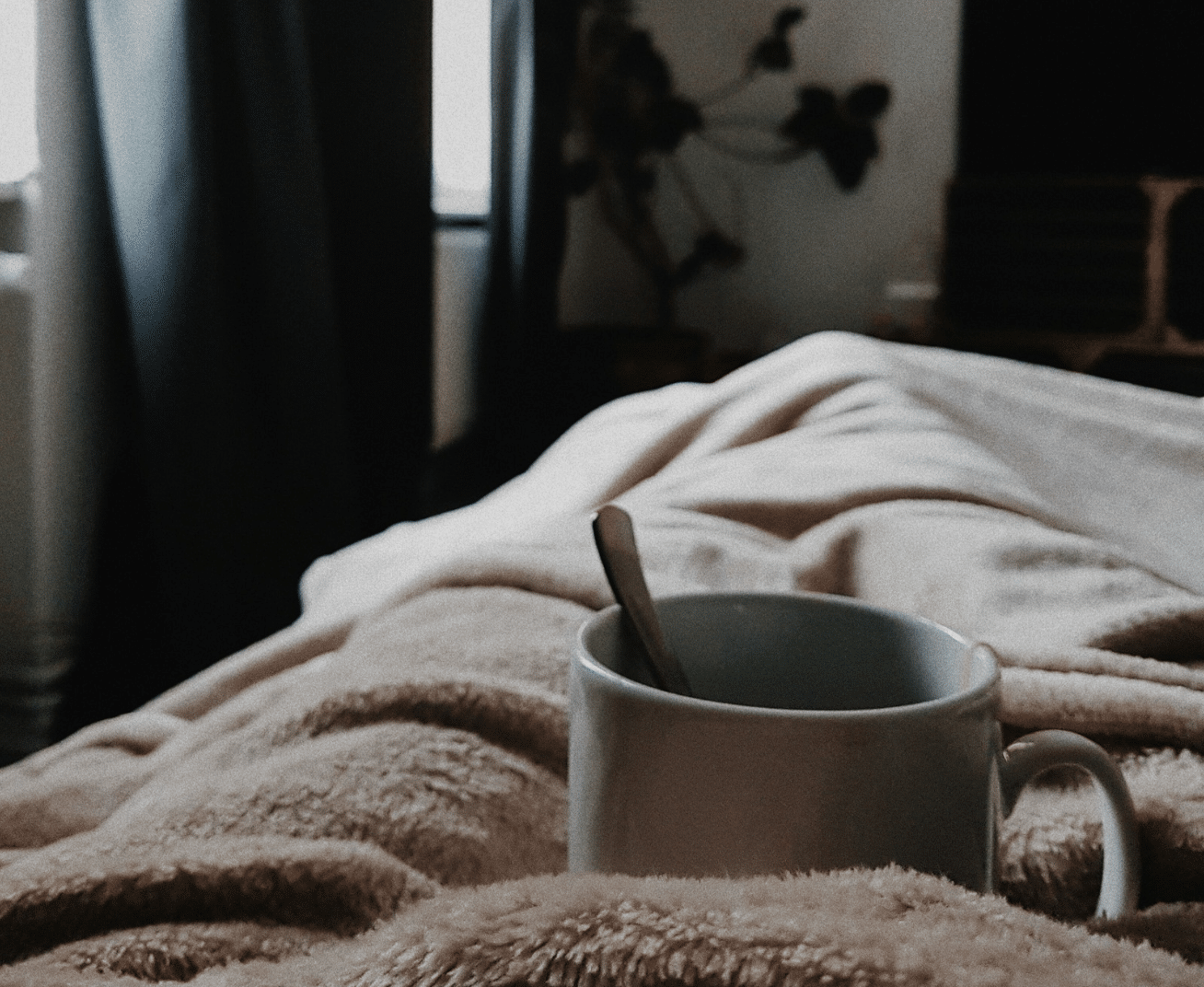 Cozy scene of a cup with a spoon resting on a soft blanket, symbolizing relaxation and self-care during holidays.